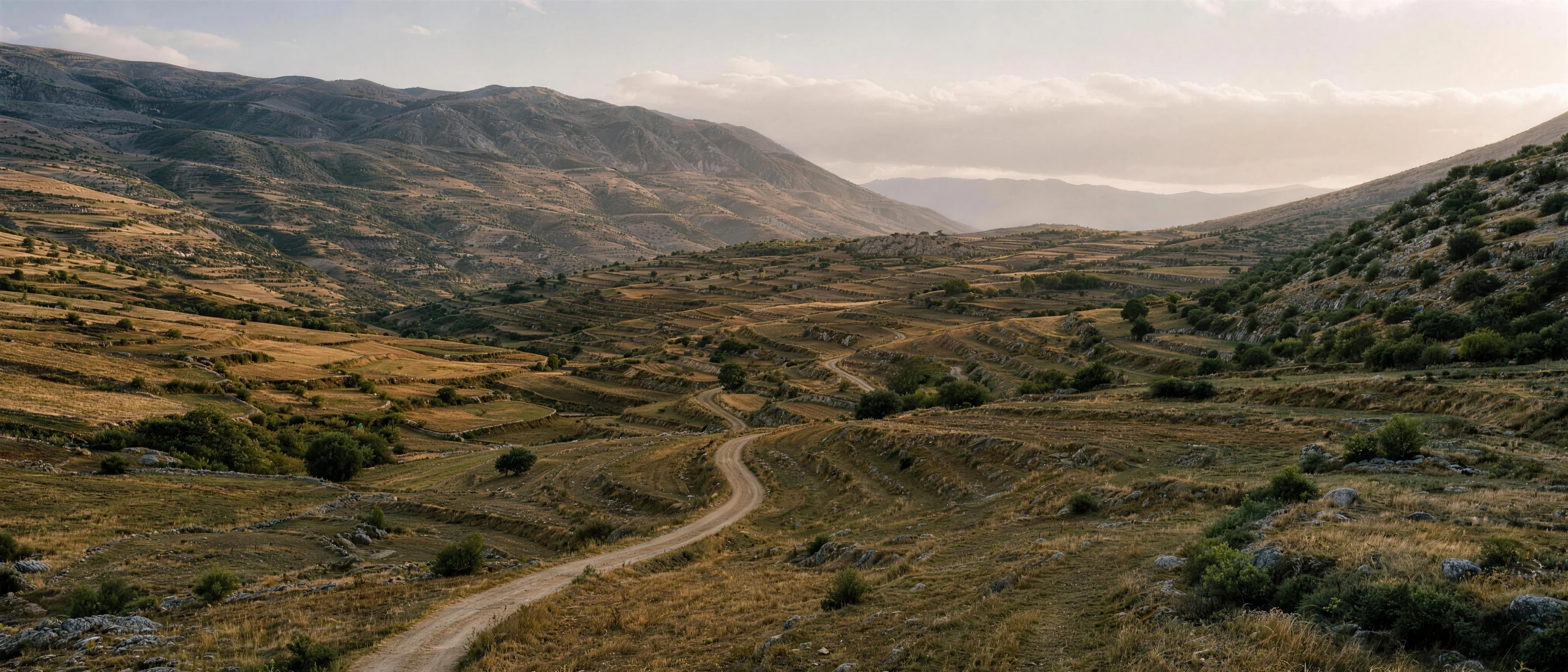 A high terraced valley with a single dirt road winding toward a distant stone village
